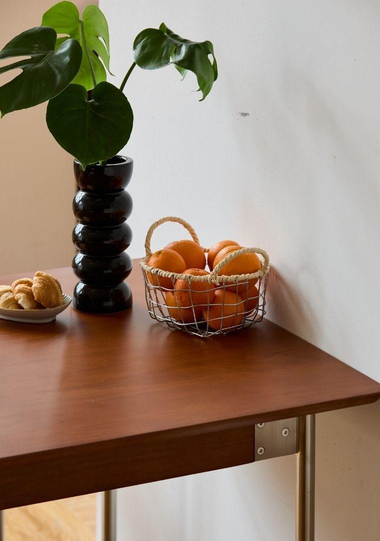 Basket of oranges on a wooden table with a plant and cookies in the background