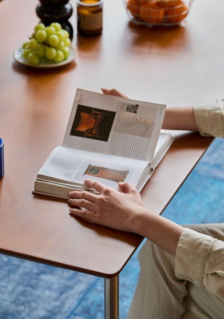 Person reading a book at a table with fruit and a pumpkin in the background