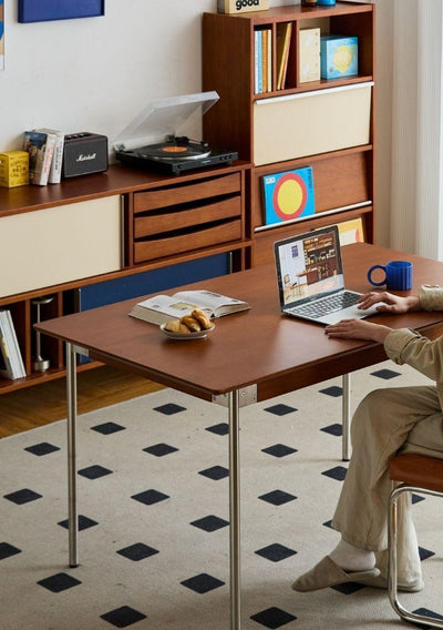 Person using a laptop at a wooden desk in a home office setting.