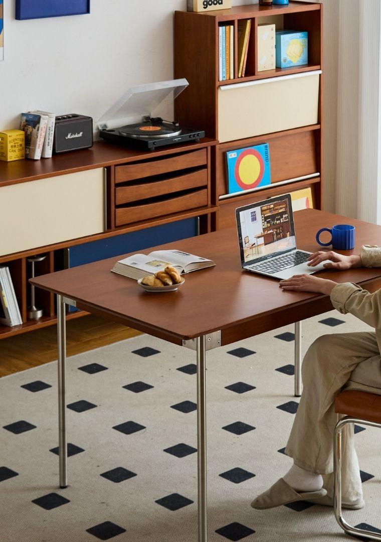 Person using a laptop at a wooden desk in a home office setting.