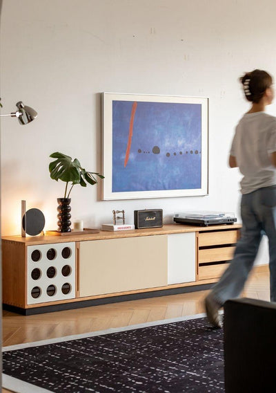 Modern living room with a wooden sideboard, abstract art, and a person walking by.