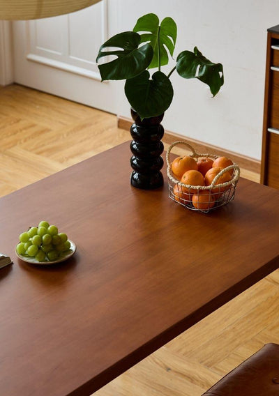 Wooden table with a vase, bowl of grapes, and basket of oranges.