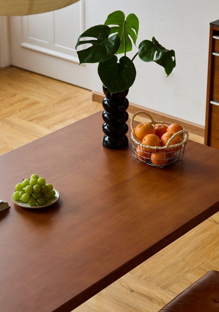Wooden table with a vase, bowl of grapes, and basket of oranges.