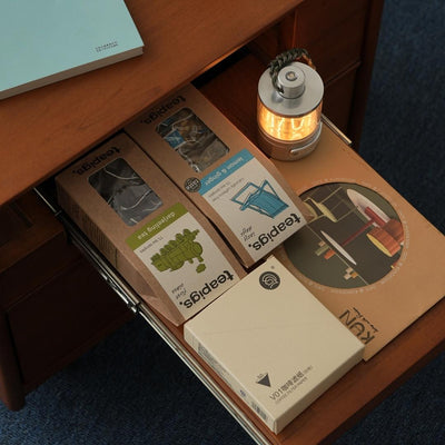 Open drawer with various items including a small lamp, boxes, and a notebook.