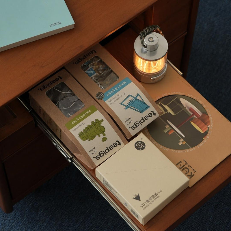 Open drawer with various items including a small lamp, boxes, and a notebook.