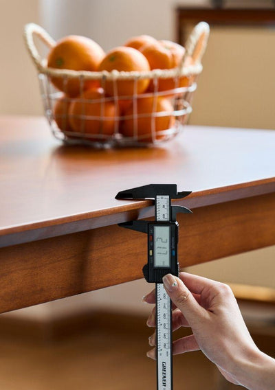 Digital caliper measuring a wooden surface with a basket of oranges in the background