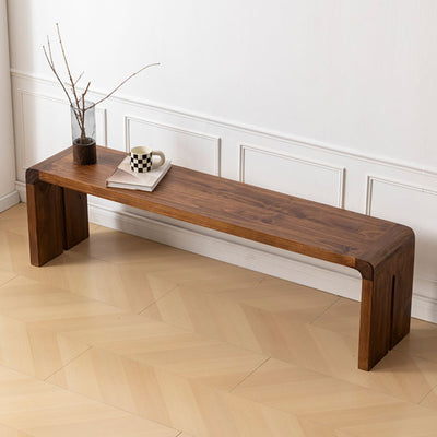 Wooden bench with a plant, mug, and book on a light wooden floor.